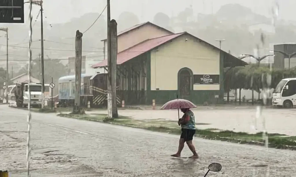 Pedestre atravessa rua sob forte chuva com guarda-chuva