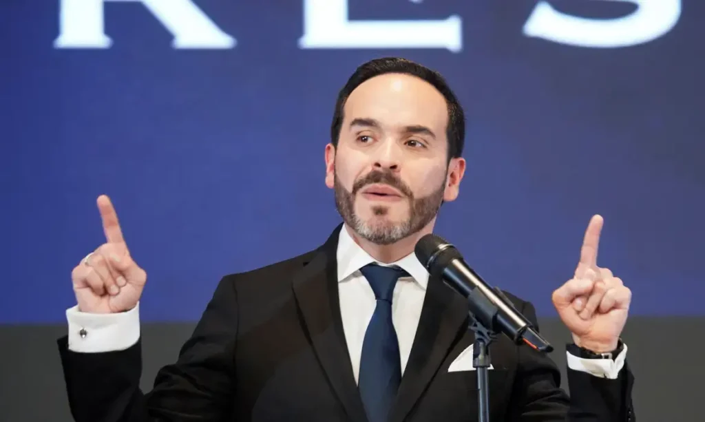 Homem de terno discursa ao microfone gesticulando com os dois indicadores